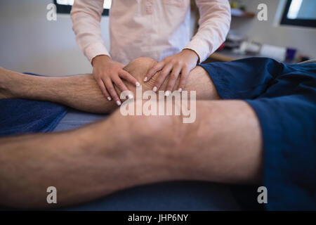 Ärztin, die Knie des Patienten am Bett liegen massieren Stockfoto