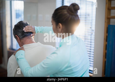 Rückansicht des weiblichen Therapeuten geben Hals massieren senior männlichen Patienten im Krankenhaus Stockfoto