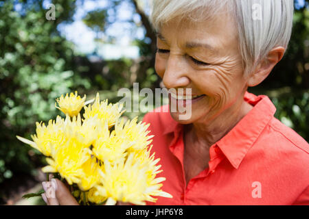 Nahaufnahme des lächelnden senior Frau betrachten frische gelbe Blumen im Garten Stockfoto