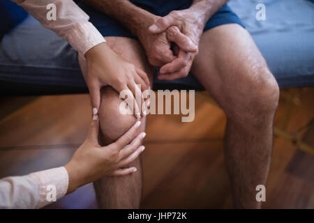 Vogelperspektive anzeigen von weiblichen Therapeuten untersuchen Knie während senior männlichen Patient sitzt am Bett auf der Krankenstation Stockfoto