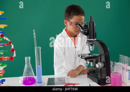 Lächelnde Schuljunge Blick durch das Mikroskop im Labor in der Schule Stockfoto
