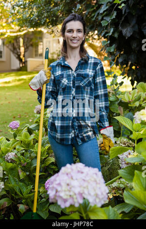 Porträt von lächelnden Frau mit Gartengeräten von Hortensie Blumen im Garten Stockfoto