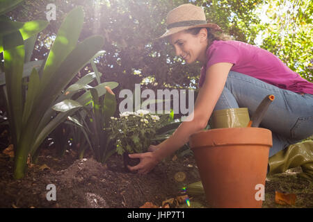 Seitlichen Blick auf lächelnde Frau pflanzt Blumen beim hocken im Hinterhof Stockfoto