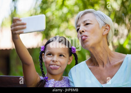 Mädchen und Großmutter, die Zunge herausstrecken, während der Einnahme von Selfie im Hinterhof Stockfoto