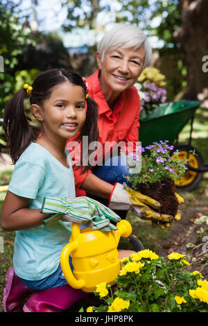 Porträt des Lächelns senior Frau und Mädchen Blumen im Garten gießen Stockfoto