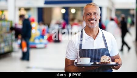 Digitalen Verbund aus Cafe Besitzer mit Kaffee und Kuchen gegen verschwommen Geschäfte Stockfoto