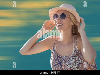 Digital Composite Frau mit Hut und Sonnenbrille vor verschwommen gelben und blauen Hintergrund Stockfoto