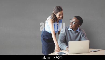 Digital Composite glücklich Geschäftsleute an einem Schreibtisch mit einem Computer vor grauem Hintergrund Stockfoto