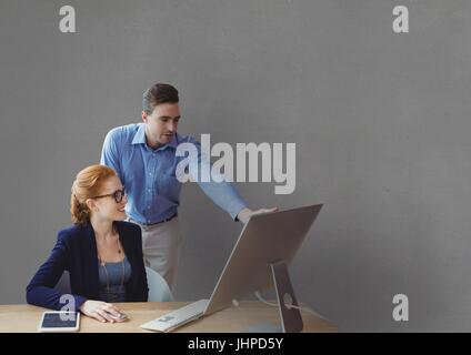Digitalen Verbund von Geschäftsleuten an einem Schreibtisch, einem Computer vor grauem Hintergrund betrachten Stockfoto