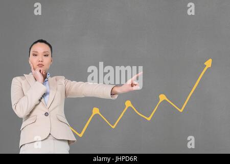 Digital Composite Business-Frau, die auf die reichen vor grauem Hintergrund mit gelber Pfeil zeigt Stockfoto