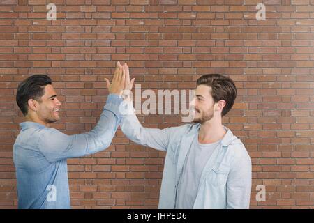 Digitalen Verbund von Happy Business-Männer, die ein high Five gegen Mauer Stockfoto