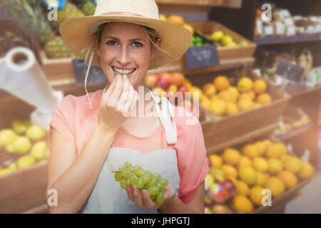 Porträt der lächelnde junge Frau essen Trauben gegen Obst im Supermarkt angeordnet Stockfoto