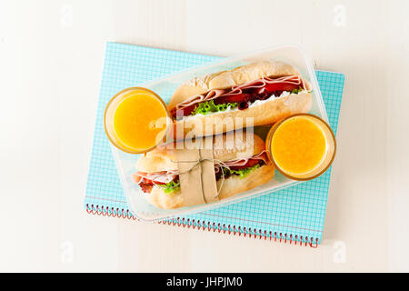Sandwich mit frischem Brot, mit italienischer Schinken und frischen Tomaten, Kopfsalat. in eine Lunchbox. Und zwei Gläser frisch gepressten Orangensaft. Schule noteb Stockfoto