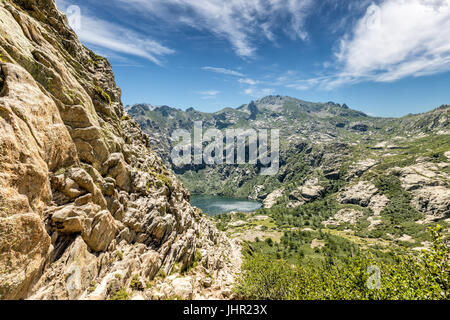 Blick hinunter auf Lac de Melo vom Wanderweg zum Lac de Capitello an der Spitze der Restonica-Tal in der Nähe von Corte in Korsika mit Felsen in der foregr Stockfoto