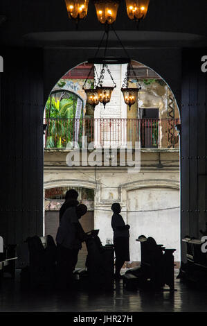 Silhouette des Menschen in der Kirche beten gesehen Trog eine offene Tür mit alten Kolonialhaus im Hintergrund Stockfoto