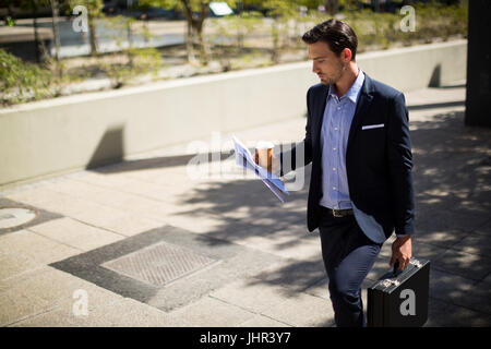 Geschäftsmann, Zeitung lesen, bei einem Spaziergang an einem sonnigen Tag im Büro-campus Stockfoto