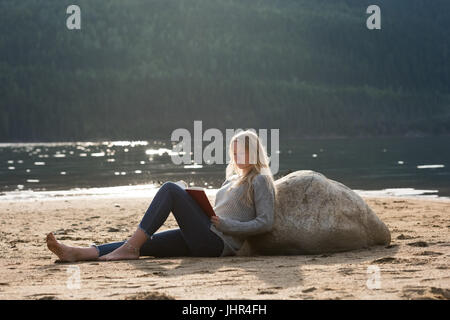 Frau liegend auf Felsen während des Lesens Roman am Seeufer Stockfoto