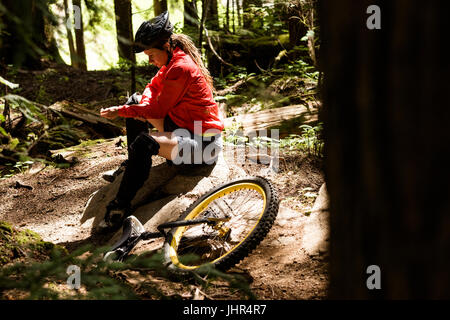 Seitenansicht der Frau sitzt auf Felsen von Einrad im Wald Stockfoto