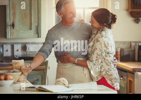 Älteres paar zärtlich umarmt, Backen und Weintrinken in Küche Stockfoto