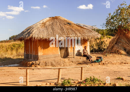 Malawische Mutter saß auf der Veranda (Khonde) ihre traditionellen Schlamm gebaut Haus im Dorf mit strohgedeckten Grasdach mit gesammelten Brennholz. Stockfoto