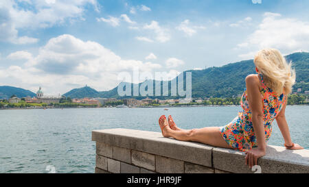 Attraktive junge Blondine am Ufer mit Blick auf den Comer See, Italien Stockfoto