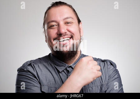 Porträt des Lachens jungen Mannes gegen graue Wand. Glücklicher Kerl Lächeln auf den Lippen. Stockfoto