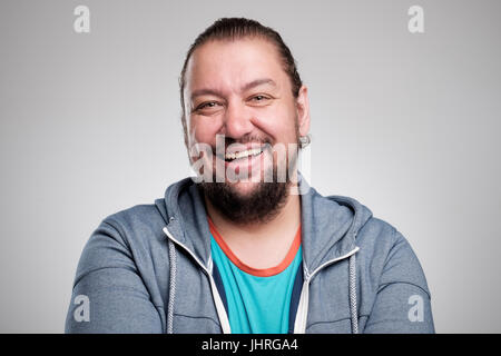 Porträt des Lachens jungen Mannes gegen graue Wand. Glücklicher Kerl Lächeln auf den Lippen. Stockfoto