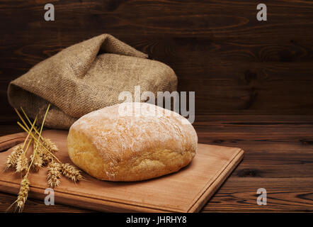 Ciabatta-Brot mit den Ohren des Weizens und Sackleinen über dunklen Holztisch Hintergrund, rustikalen Stil, Nahaufnahme Stockfoto