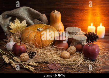 Herbst dunklen Thanksgiving-Konzept mit Kürbissen, roter Apfel, Knoblauch, Kegel, Nuss, Krug, Stroh und brennenden Kerzen auf Holztisch, Grußkarte Stockfoto