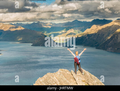 Weibliche Wanderer auf einem Felsen, streckte die Arme in die Luft, Lake Hawea und Berglandschaft, Isthmus Peak, Otago, Südinsel Stockfoto