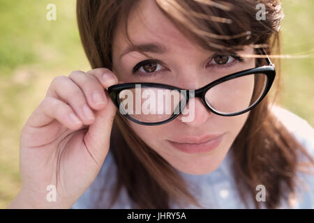 Schöne junge Frau Anpassung ihrer Brille und Lächeln Sie über erlauben grünen Hintergrund. Stockfoto