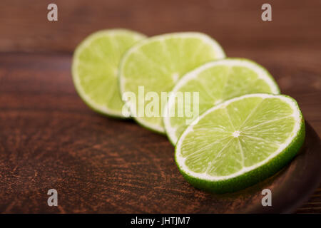 Limettenscheiben auf einer dunklen Platte auf dem hölzernen Hintergrund Stockfoto