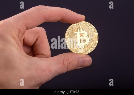 Mannes Hand mit goldenen Bitcoin auf schwarzem Hintergrund Stockfoto