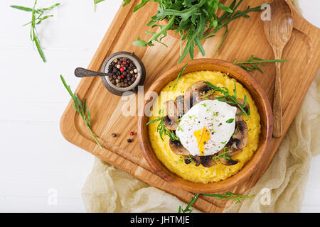 Frühstück. Polenta mit Pilzen und pochiertem Ei. Flach zu legen. Ansicht von oben. Stockfoto