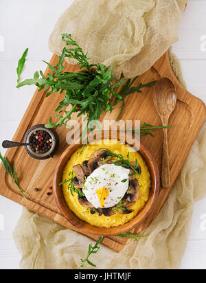 Frühstück. Polenta mit Pilzen und pochiertem Ei. Flach zu legen. Ansicht von oben. Stockfoto