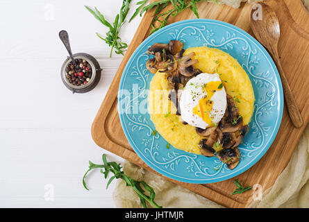 Frühstück. Polenta mit Pilzen und pochiertem Ei. Flach zu legen. Ansicht von oben. Stockfoto