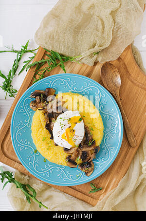 Frühstück. Polenta mit Pilzen und pochiertem Ei. Flach zu legen. Ansicht von oben. Stockfoto