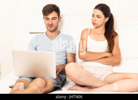 Süchtig junge Mann auf dem Bett mit einem Laptop, während die Frau wütend sieht Stockfoto