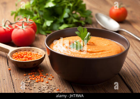 Suppe-Püree von roten Linsen in eine braune Schale, frische Tomaten, Petersilie auf einem alten hölzernen Hintergrund Stockfoto