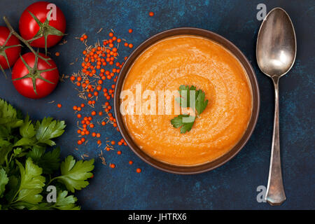 Suppe-Püree von roten Linsen in eine braune Schale, frische Tomaten, Petersilie auf blauem Grund. Ansicht von oben Stockfoto