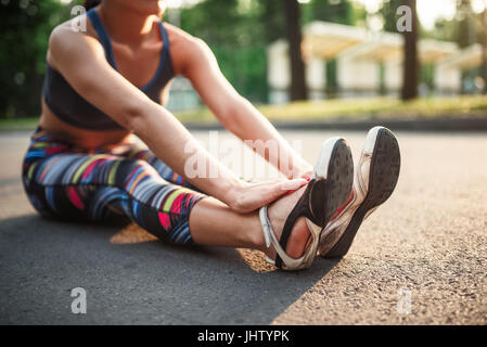 Sportliche Mädchen sitzen auf Bürgersteig in grünen Sommerpark. Frau am morgendlichen Workout entspannen Stockfoto