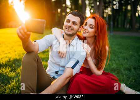 Liebespaar macht Selfie auf Handy-Kamera im Sommerpark am Sonnenuntergang. Romantisches Date attraktive Frau und junger Mann Stockfoto