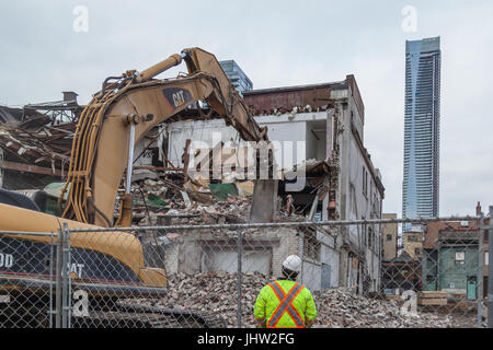 TORONTO, KANADA, 28. NOVEMBER 2016: Ein Bauarbeiter überwacht den Abriss eines alten Gebäudes mit einem neuen Hochhaus im Hintergrund. Stockfoto
