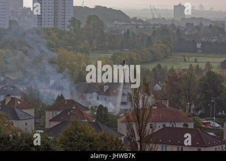 Feuerwehrleute kämpfen Feuer hoch auf Leiter in Glasgow Knightswood Vorort Haus Feuer Sonnentag Stockfoto