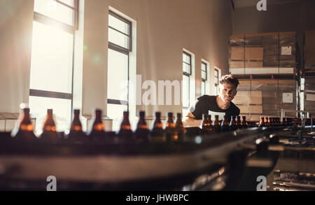 Brewer, Förderband mit Bierflaschen zu betrachten. Junger Mann, Überwachung der Herstellung von Bier im Brauerei-Werk. Stockfoto