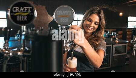 Schöne junge Frau Bier in das Glas gießen. Weiblichen Barkeeper Antippen Handwerk Bier in der Bar. Stockfoto