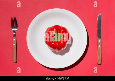 Draufsicht der rote Paprika auf weißen Teller mit Messer und Gabel auf rotem Grund Stockfoto