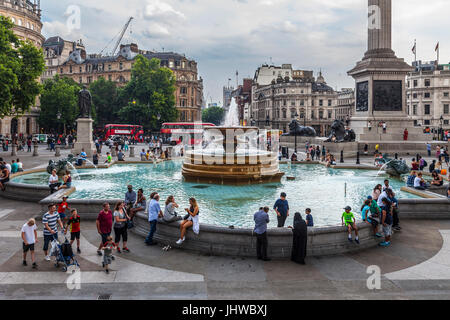 Touristen und Einheimische, Familien und Freunde um einen Brunnen am Trafalgar Square im Zentrum von London, England. Stockfoto