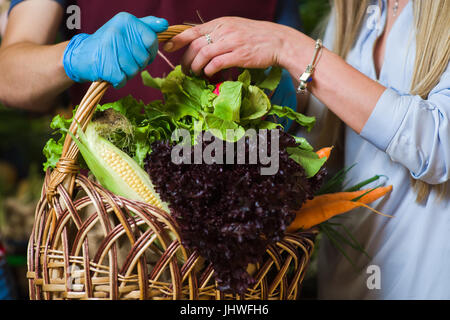 Der Verkäufer und der Käufer mit einem Korb mit verschiedenen Gemüse am Bauernmarkt. Stockfoto