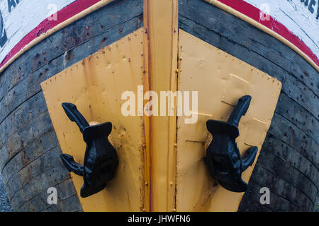 Zwei schwarze Anker ruht gegen schützende Metallplatten auf die Bogen auf einem Holzboot Stockfoto